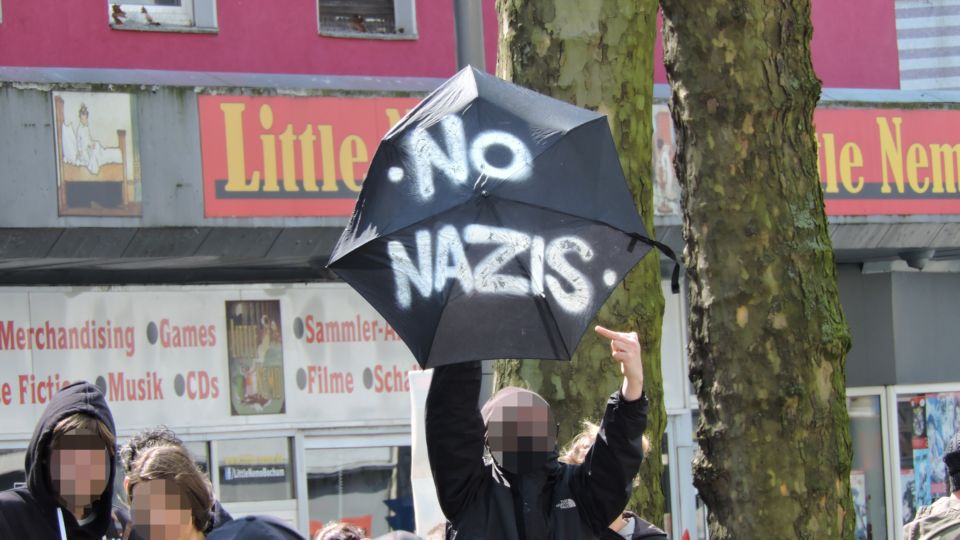 Demonstrant zeigt einen geöffneten Schrim auf dem "No Nazis" steht.