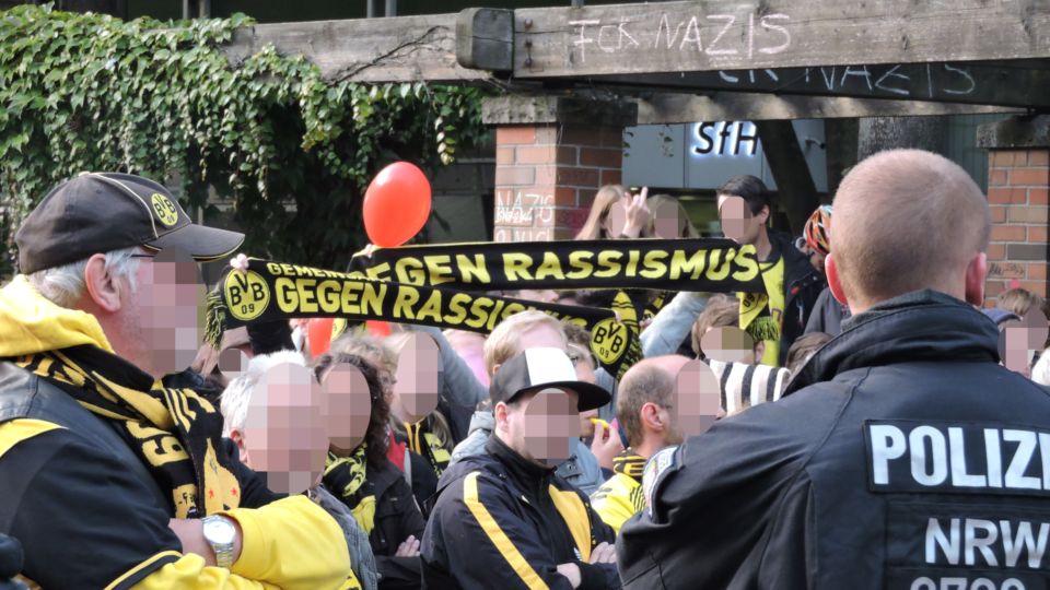 Bild vom Gegenprotest. Menschen mit BVB Schals auf denen "Gegen Rassismus" steht.
