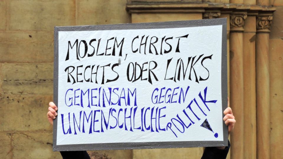 Schild mit Text "Moslem, Christ, Links oder Rechts, gegen unmenschliche Politik".